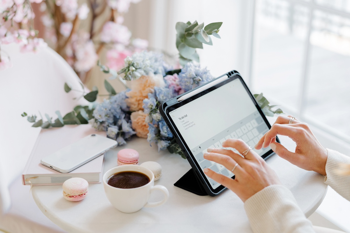 Fingers typing on a tablet near wedding flowers and coffee on a table