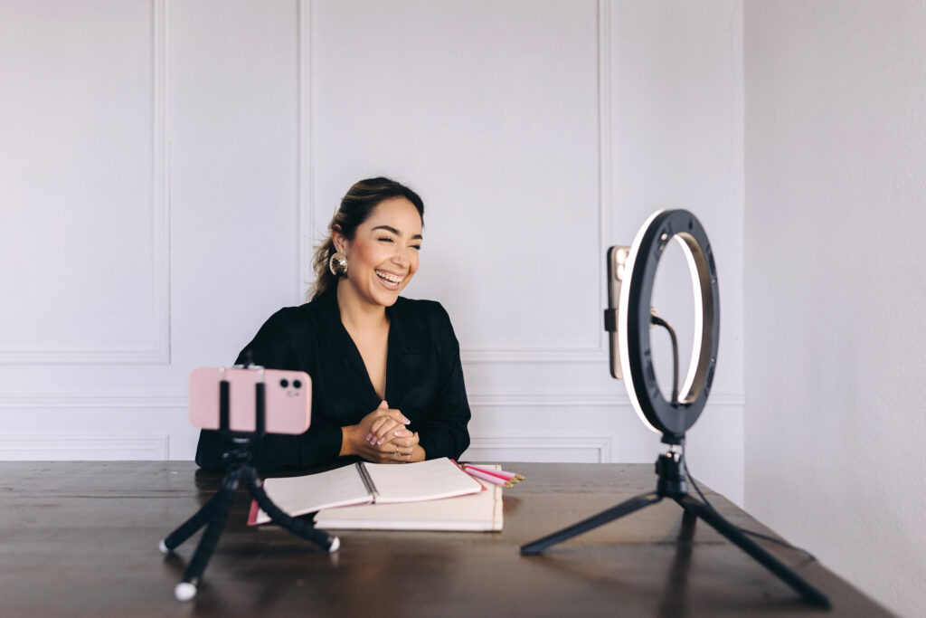 woman sitting at desk with laptop and ring light and video recording equipment