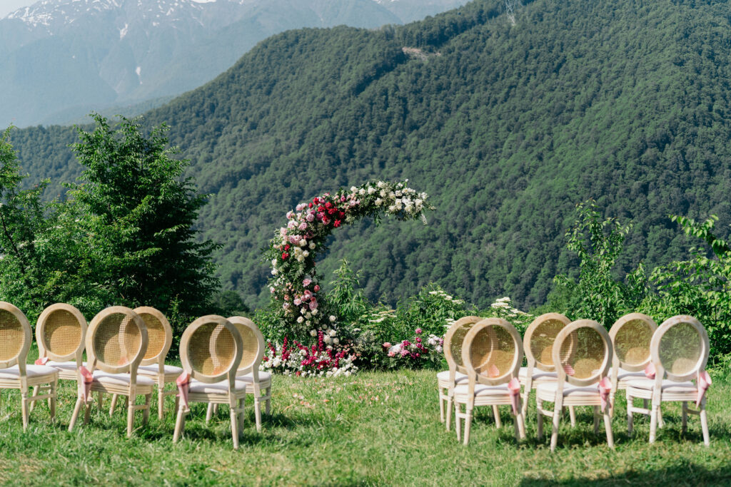 a sprawling green mountain view with a luxury outdoor wedding setup including a floral installation with pink and white flowers