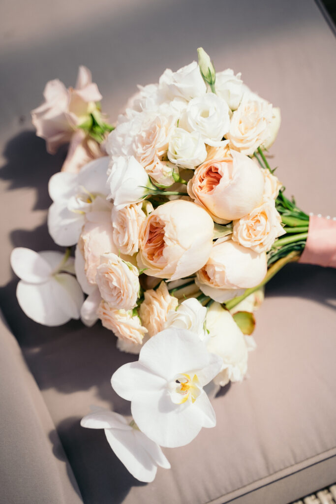a wedding bouquet of white and peach flowers laying on a cushion