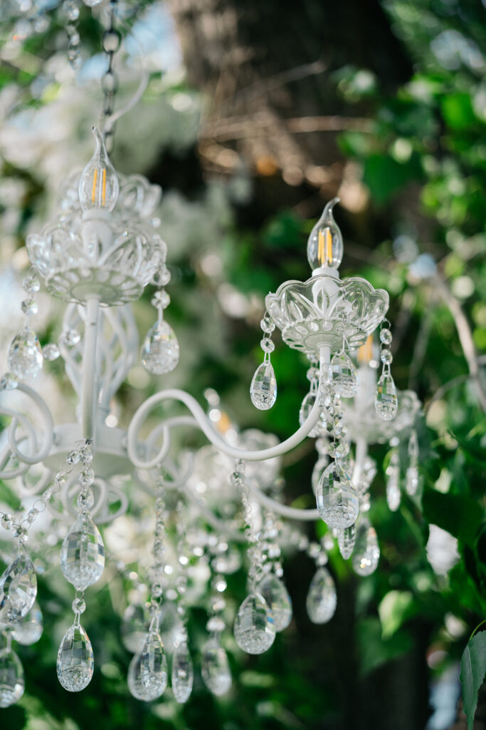 glass chandelier hanging from green-leafed trees for a luxury outdoor wedding reception