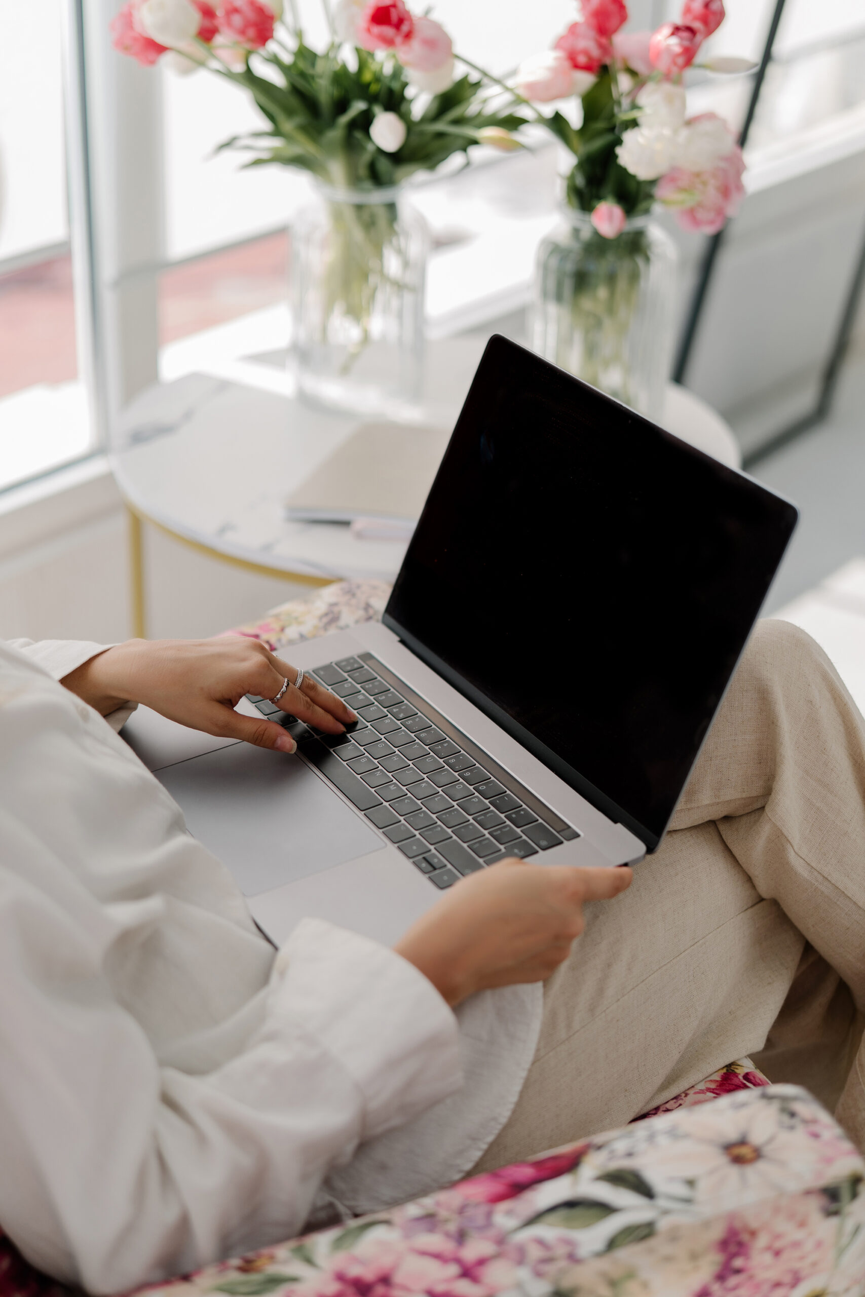 a woman with a laptop on her lap surrounded by pink flowers